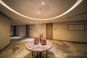 A hotel corridor with a round table featuring two metallic vases with branches, a curved ceiling with recessed lighting, and a framed sign on the wall. - Yi Yuan Hotel (Wuxi)