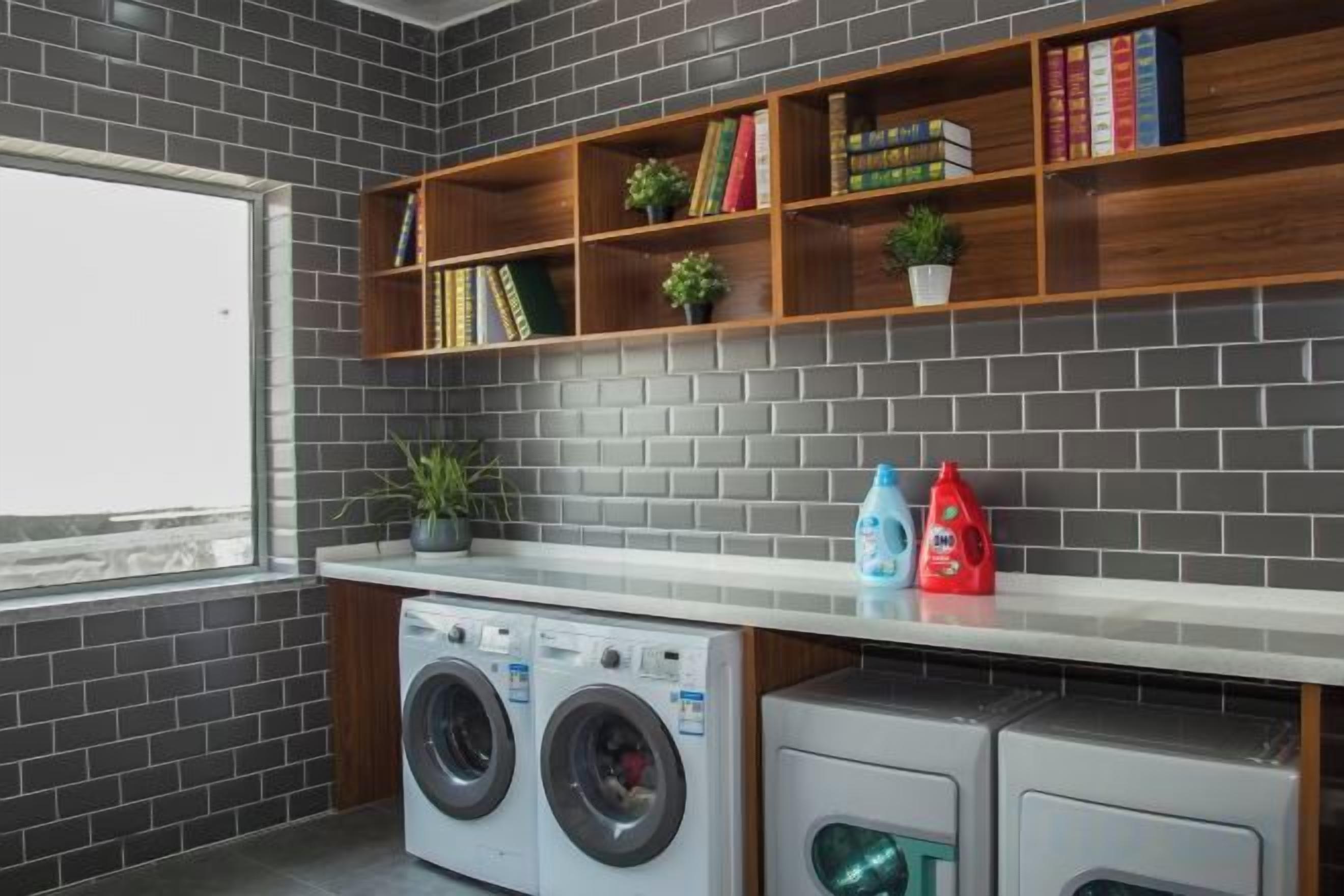 Un área de lavandería con lavadora, secadora y estantes con libros y plantas.