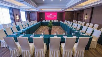 A conference room with a long table, white chairs, and a stage with a red backdrop.