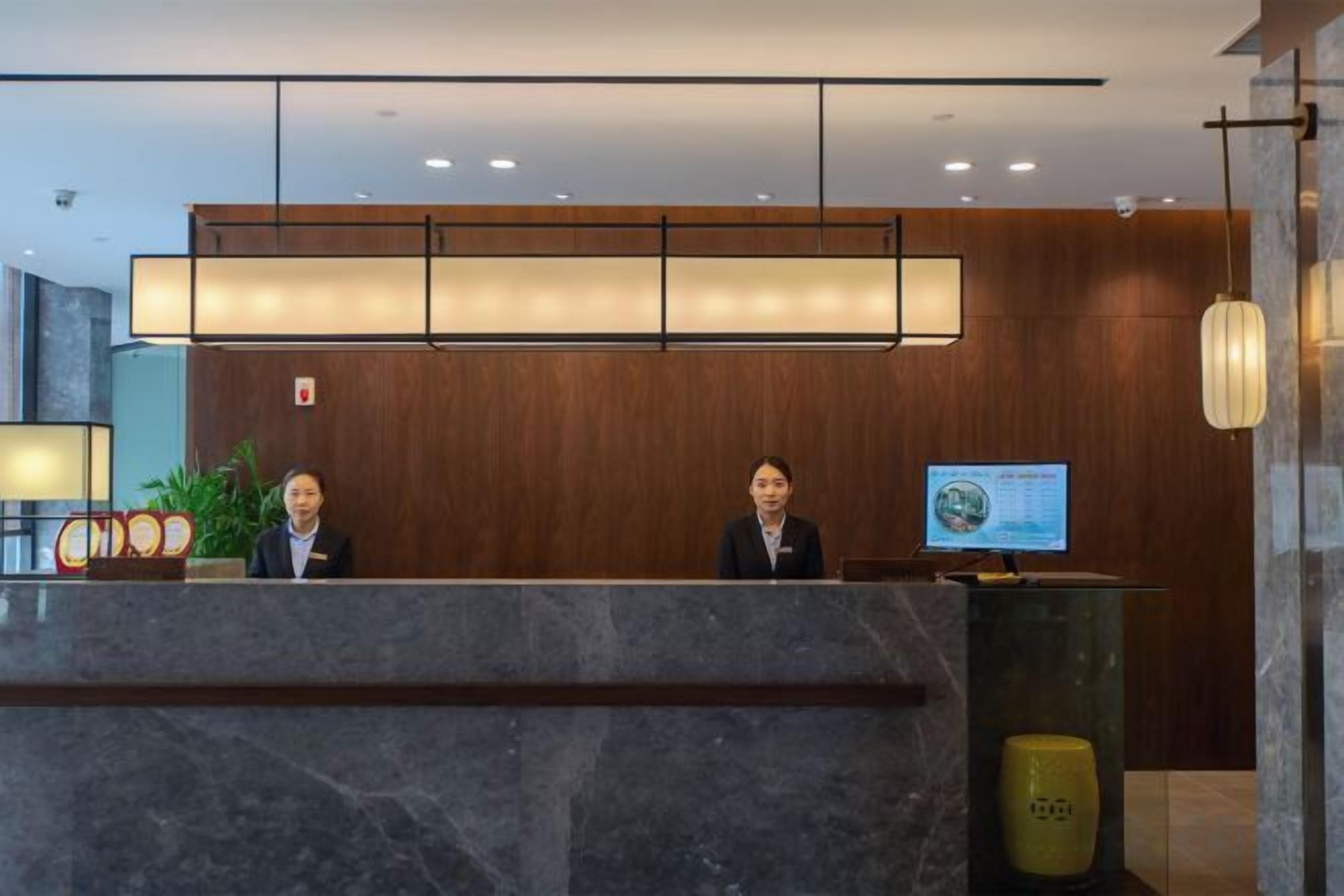 Una recepción con dos empleados, una pantalla digital y una planta.