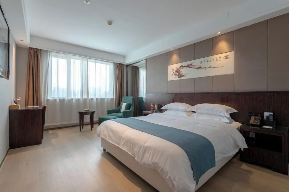 A hotel room with a large bed, a bedside table, a chair, and a desk with a lamp.