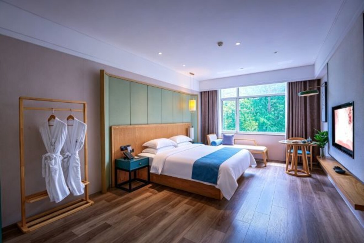 Une chambre d’hôtel avec un grand lit, des tables de chevet, une télévision et une fenêtre donnant sur des arbres.