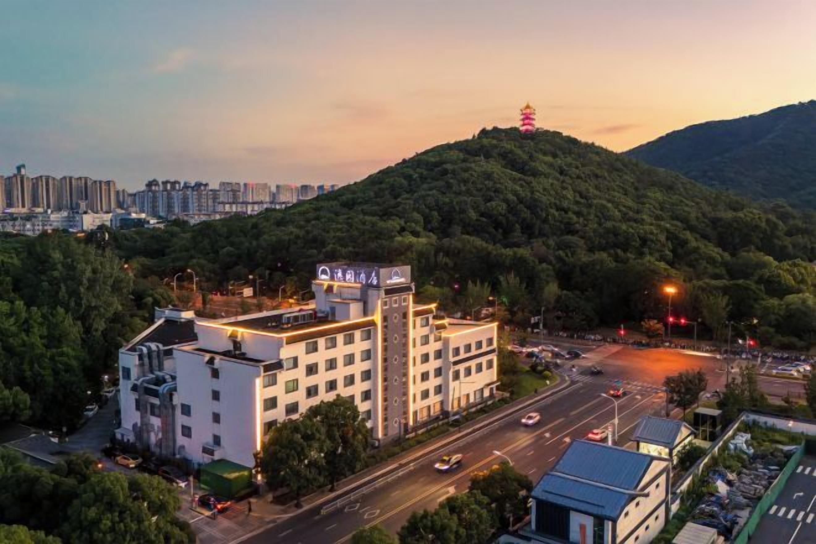 A hotel with multiple floors, surrounded by greenery and a hilly landscape.