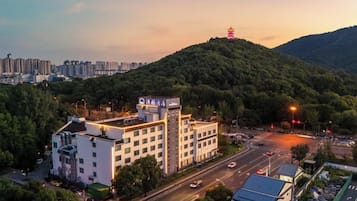 A hotel with multiple floors, surrounded by greenery and a hilly landscape.