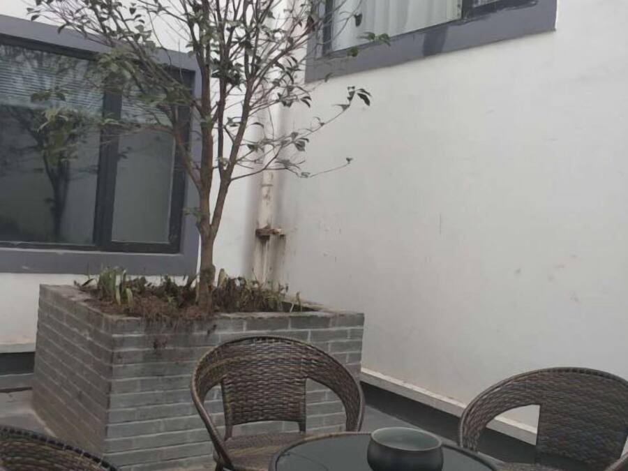 A patio with wicker chairs and a table, a small tree, and a white wall.