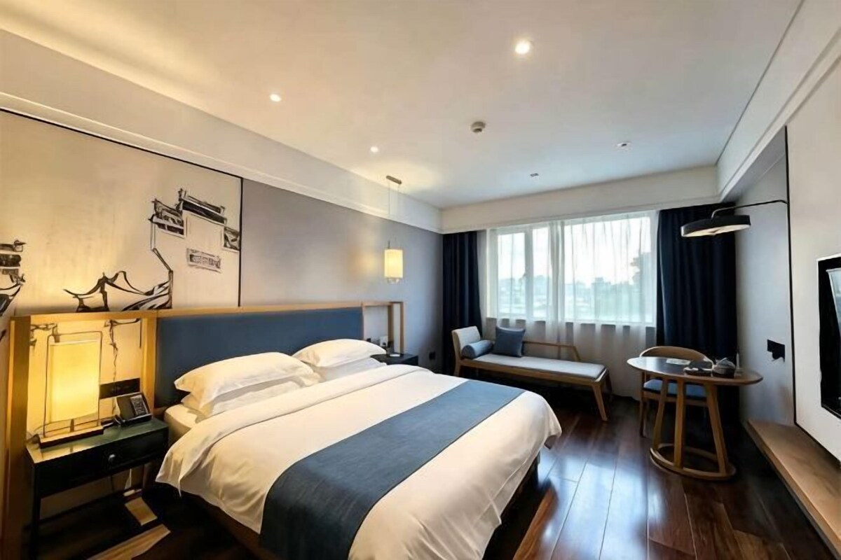 A hotel room with a bed, bedside table, lamp, seating area, and a TV.