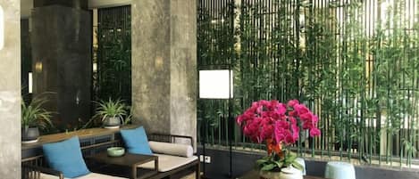 A modern indoor seating area with sofas and a table, surrounded by tall bamboo plants and a large window.