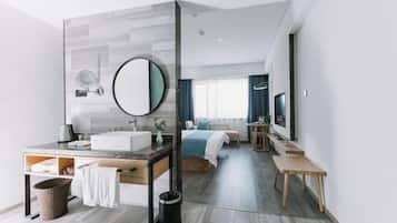 A modern hotel room with a large mirror, a sink, a bedside table, a bed, a TV, and a window with curtains.