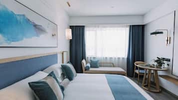 A modern hotel room with a large bed, a seating area with a table, and a large window with curtains.