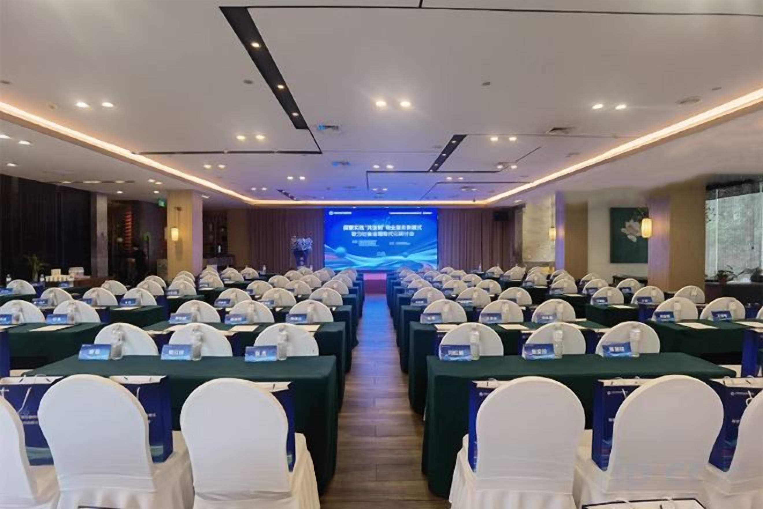 A conference room with rows of tables and chairs, a stage with a presentation screen, and a podium.