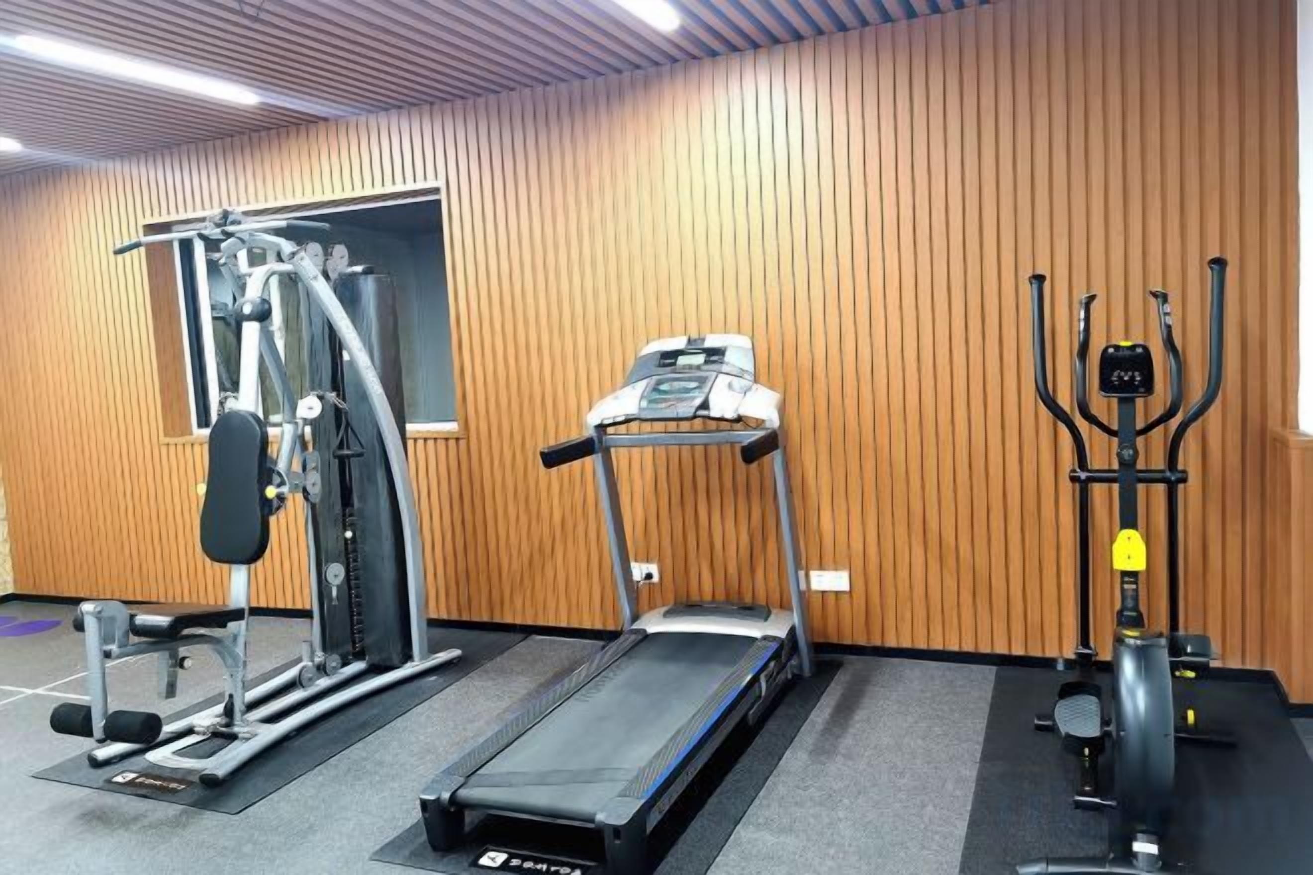 Un gimnasio con cinta de correr, máquina de pesas y máquina de poleas.