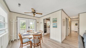 A spacious room with a dining table and chairs, a ceiling fan, and a view of the kitchen and living area.