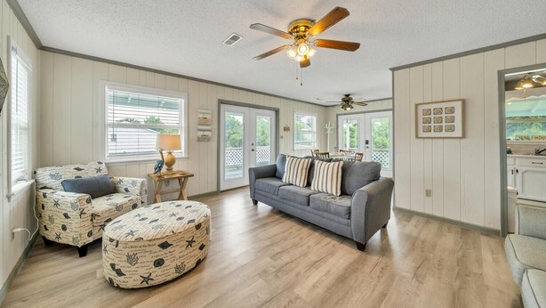 A spacious living room with a grey sofa, patterned ottoman, and a ceiling fan.