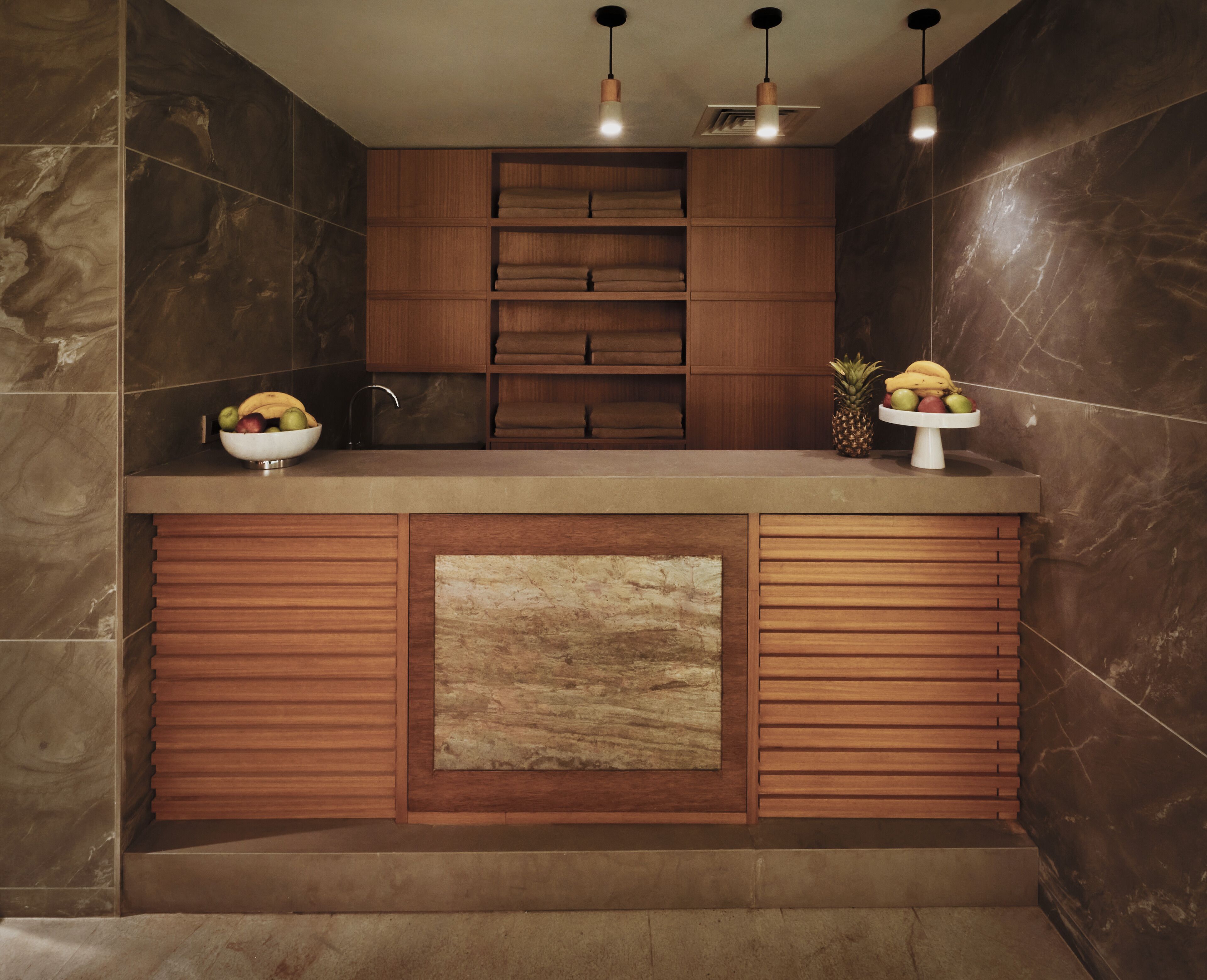 A modern kitchen with a marble backsplash, wooden cabinets, and a central island with a bowl of fruit.