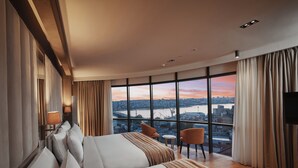 A hotel room with a large bed, two bedside tables, a TV, and a view of a cityscape through large windows. - Grand Galata Hotel & Spa - Special Class (Istanbul)