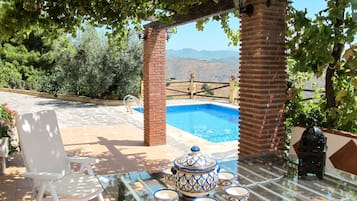 Un área de piscina con una mesa de vidrio, sillas y una maceta decorativa.