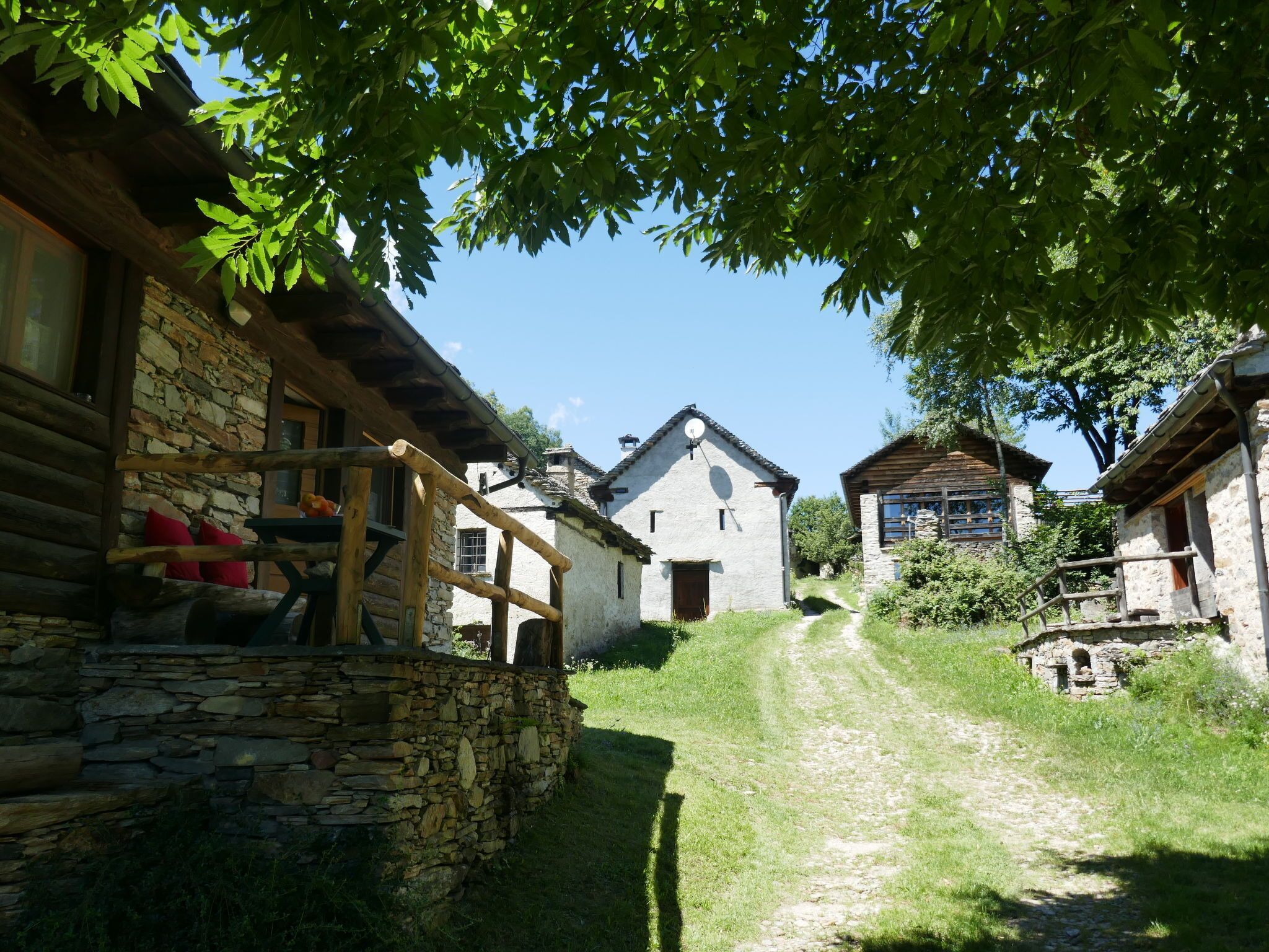 A rustic village with stone buildings, a wooden porch, and a clear path leading through the area.