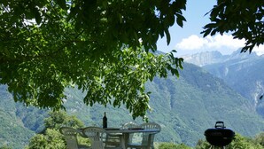 An outdoor dining area with a table and chairs, a bottle of wine, and a grill, set against a mountainous backdrop. - Rustico Ingrid (MVA338) by Interhome (Malvaglia)