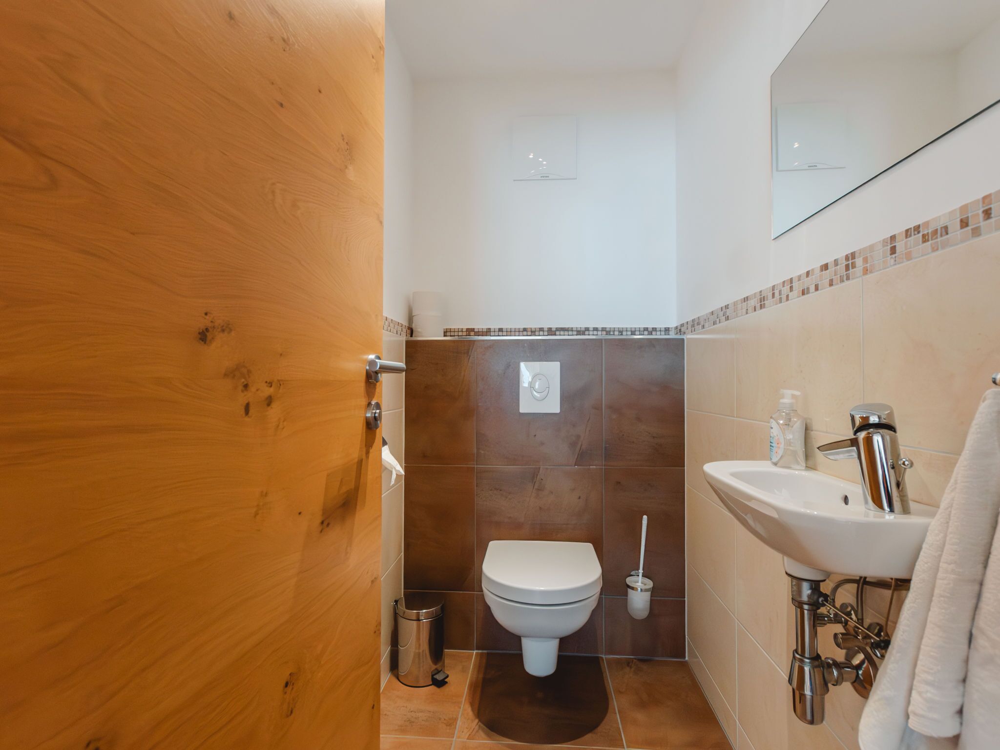 Une salle de bain avec une porte en bois, des toilettes, un lavabo et un miroir.