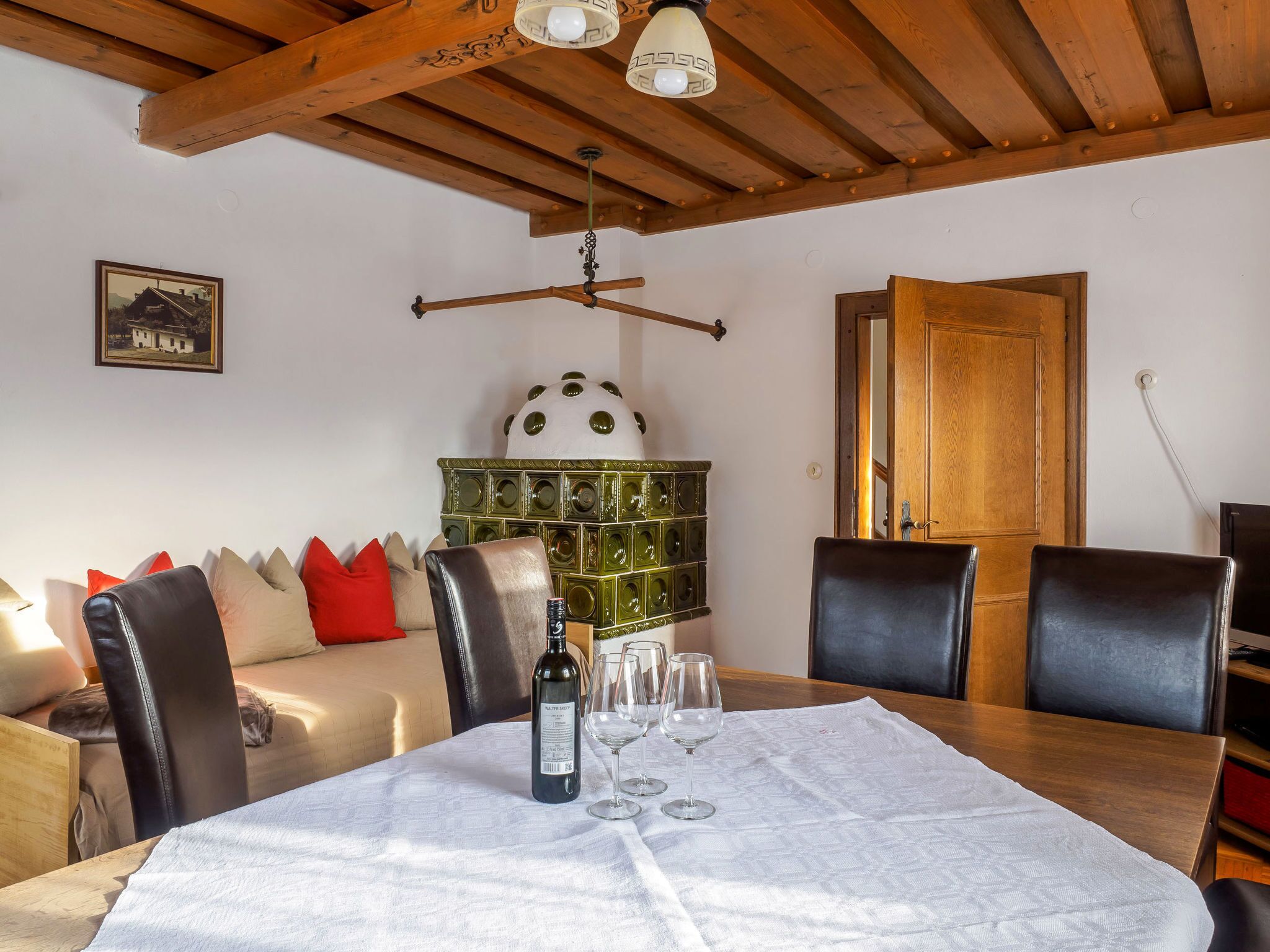 Un coin repas avec une table dressée pour quatre personnes, un plafond en bois, un élément décoratif vert et une porte visible au fond.