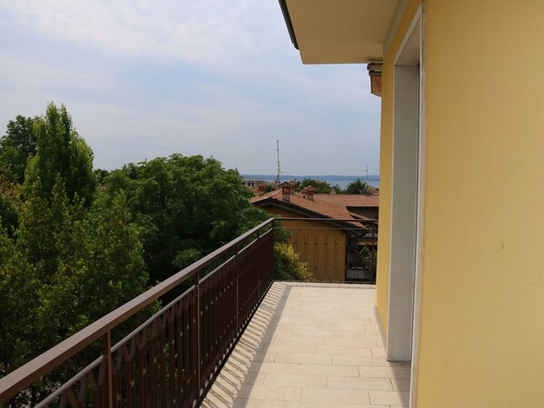 A balcony with a tiled floor, a metal railing, and a view of trees and buildings in the distance.