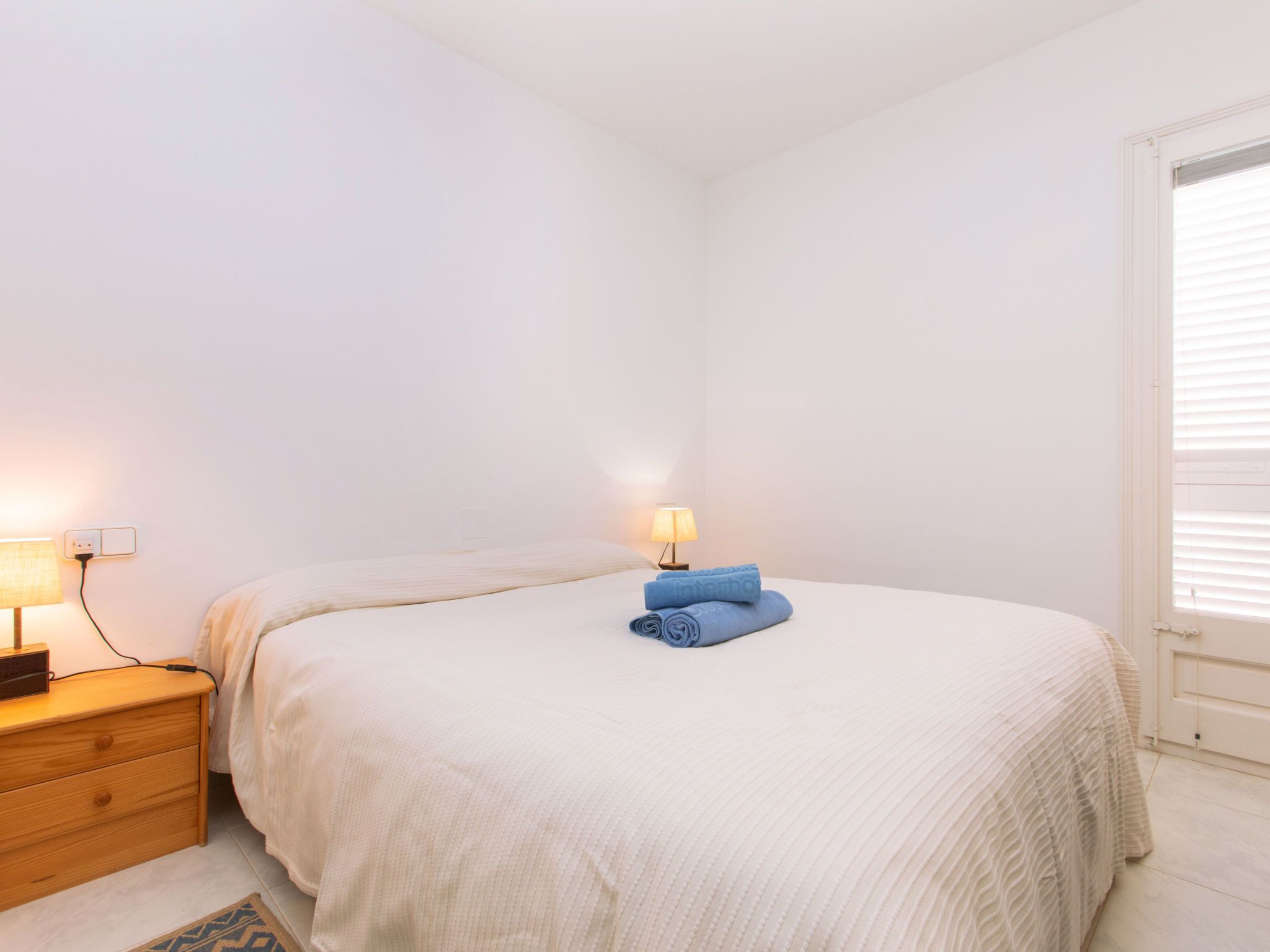 A bedroom with a bed, a nightstand, a lamp, and a window with blinds.