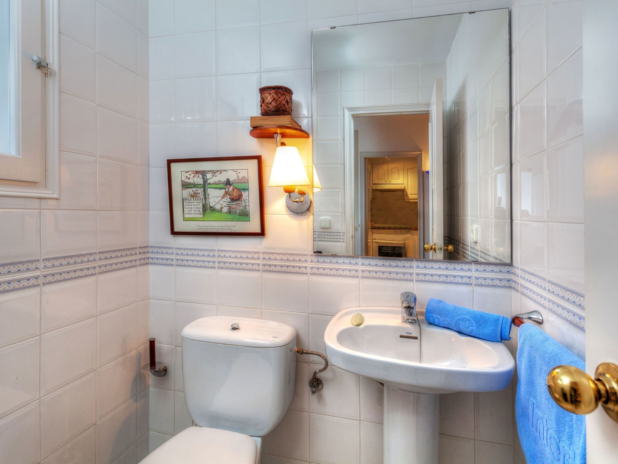 A bathroom with a toilet, sink, and a framed picture on the wall.