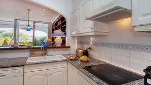 Cozinha moderna com armários brancos, bancada de granito, forno embutido e janela com vista para o verde.