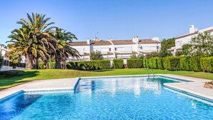 Una piscina con agua cristalina azul, rodeada de césped cuidado y palmeras.