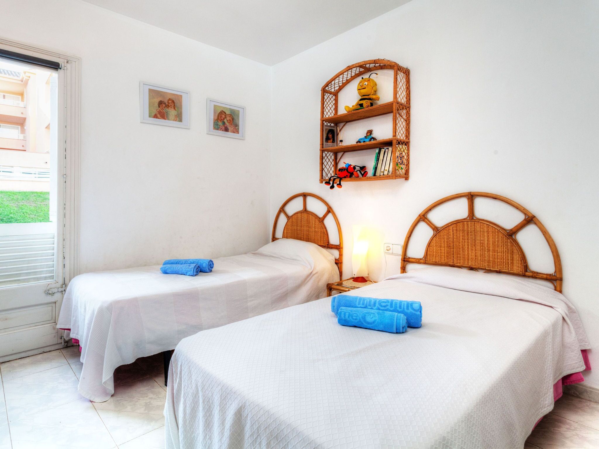 Una habitación con dos camas individuales, un estante con juguetes y una ventana con persianas.