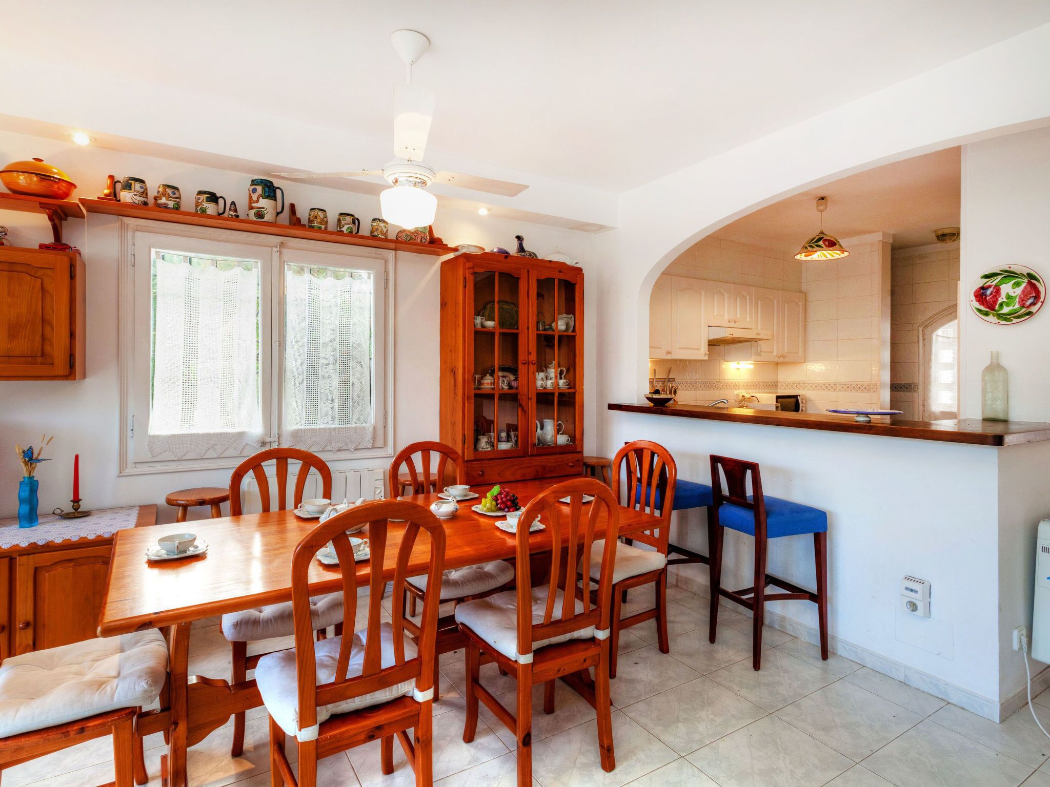 A dining area with a wooden table and chairs, a cabinet with glass doors, and a kitchen area visible through an archway.