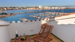 A balcony with a wooden table, a bottle of champagne, and a wooden chair. The balcony overlooks a marina with boats and buildings in the background. - Port L'escala by Interhome (L'Escala)