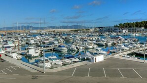 Un puerto deportivo con numerosos barcos amarrados, cielo despejado y una cadena montañosa distante.