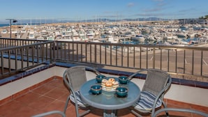 Un balcón con una mesa dispuesta para dos, con vistas a un puerto deportivo lleno de barcos.