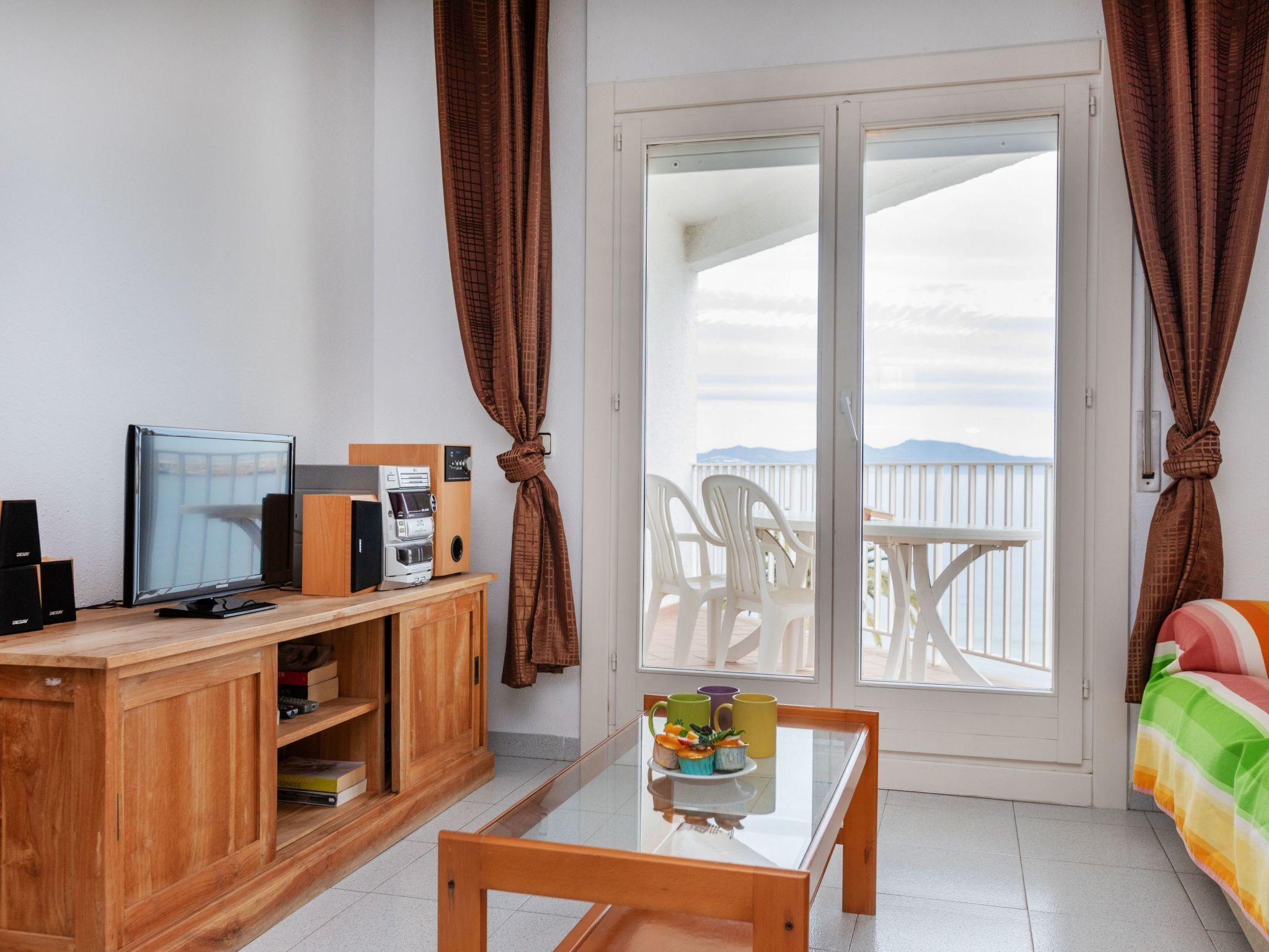 Une chambre dotée d’un bureau en bois, d’une télévision et d’une machine à café. Elle comprend également un balcon avec une table et des chaises.
