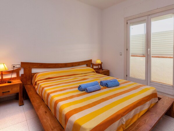 A bedroom with a wooden bed, striped bedding, two bedside lamps, and a view of the sea through a sliding door. - Riells Park by Interhome (L'Escala)