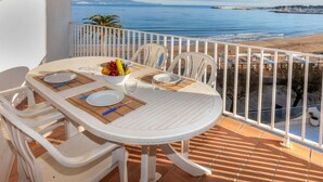 A round table with white chairs and a white tablecloth, set on a balcony overlooking a beach and the sea. - Riells Park by Interhome (L'Escala)