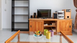 A modern living room with a glass-top coffee table, a television, speakers, and a bookshelf. - Riells Park by Interhome (L'Escala)