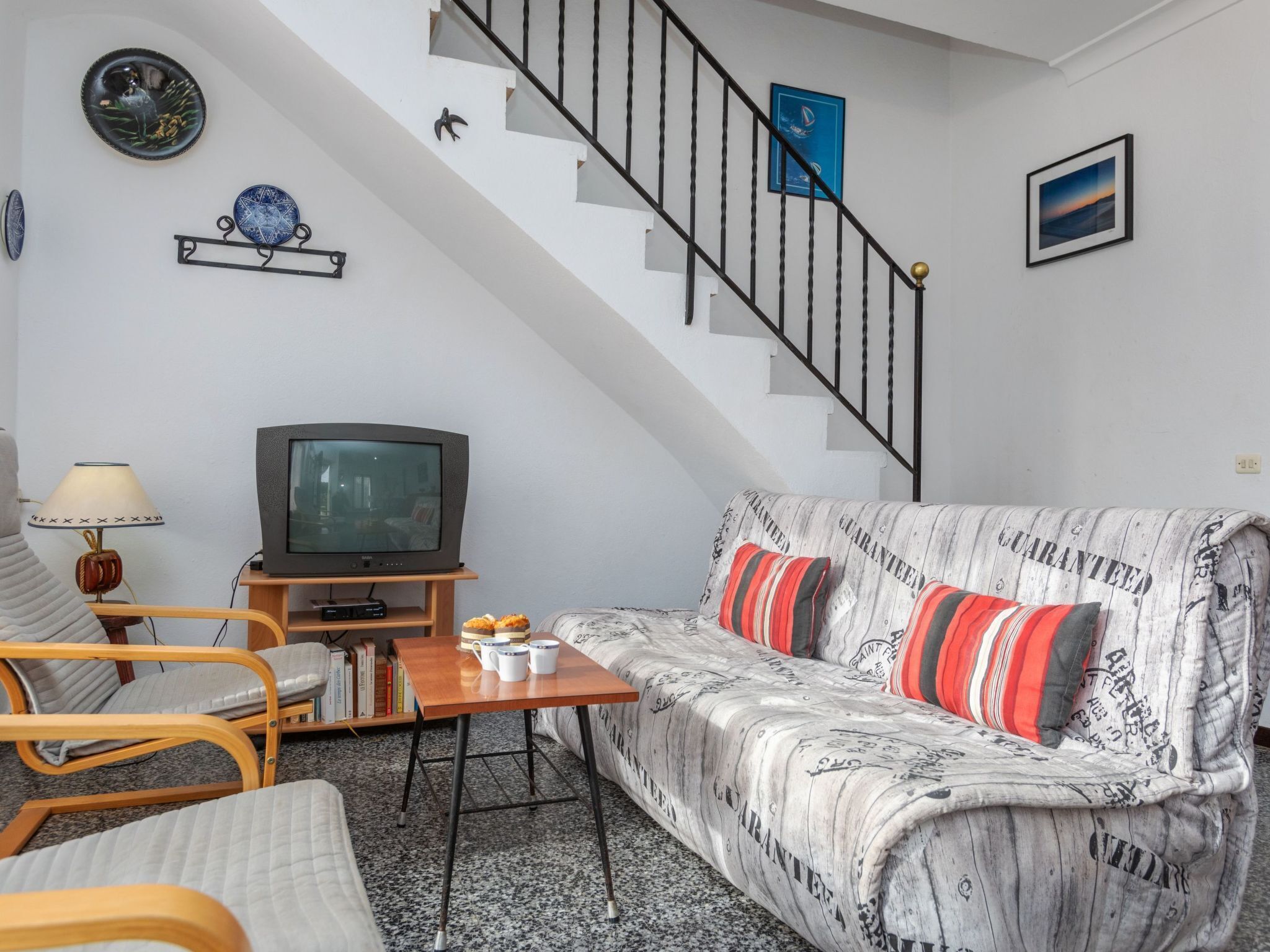 Een woonkamer met een bank, een televisie, een salontafel en een trap.