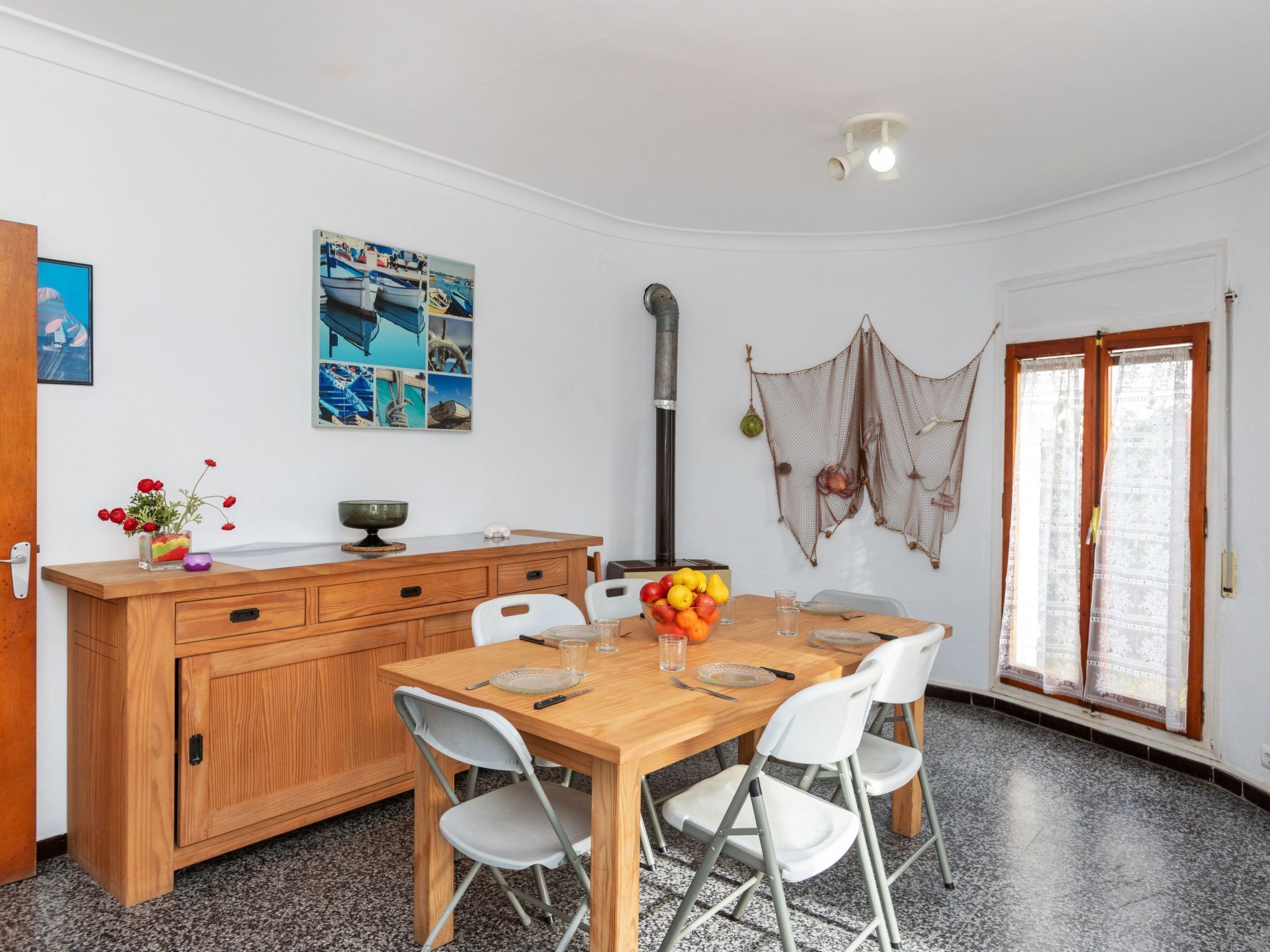 Cocina compacta con una mesa de madera, sillas blancas y un frutero.