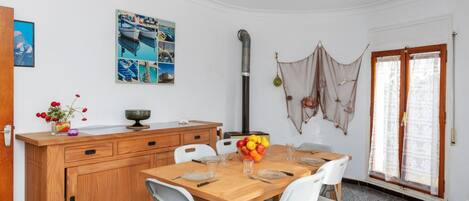 Cocina compacta con una mesa de madera, sillas blancas y un frutero.