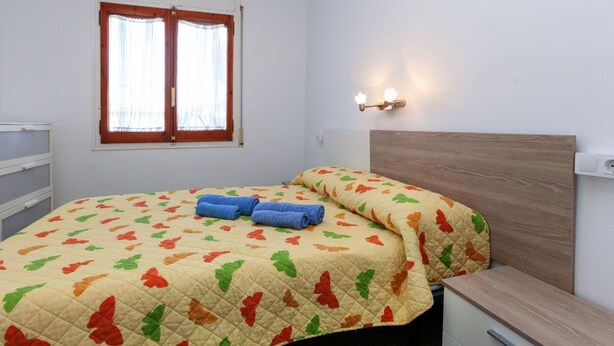 Quarto com cama, mesa de cabeceira, janela com cortinas e luminária na parede.