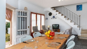 Uma sala de jantar com uma mesa de madeira posta para quatro pessoas, uma televisão e uma escada.