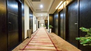 Un pasillo de hotel con piso alfombrado, puertas de madera oscura y una planta en maceta.