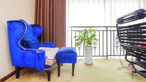 Una habitación con un sillón azul, un pequeño banquillo, una planta en maceta y un banco de metal negro.