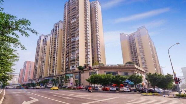 Un edificio residencial alto con varios balcones, un paso de peatones y un cielo despejado.