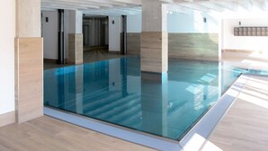 A modern indoor swimming pool with clear glass walls, wooden flooring, and a high ceiling with exposed beams. - Mariandl am Meer by Interhome (Ostseebad Binz)