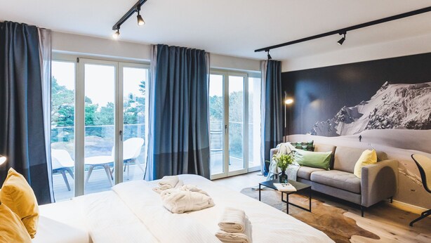 A modern hotel room with a large bed, a sofa, a coffee table, and a view of the outdoors. - Mariandl am Meer by Interhome (Ostseebad Binz)