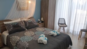 A neatly made bed with patterned bedding, a bedside table with a lamp, a wardrobe, and a chair by a window with sheer curtains. - HOUSE NEAR THE BEACH (MILITSA 🌺 ANGELIKI)
 ❤️OUR LITTLE PARADISE❤️🌺 🌺   🇨🇾 (Perivolia Larnakas)