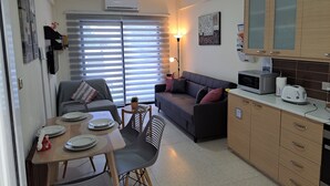 A compact living space with a dining area, sofa, kitchenette, and a large window with blinds. - HOUSE NEAR THE BEACH (MILITSA 🌺 ANGELIKI)
 ❤️OUR LITTLE PARADISE❤️🌺 🌺   🇨🇾 (Perivolia Larnakas)